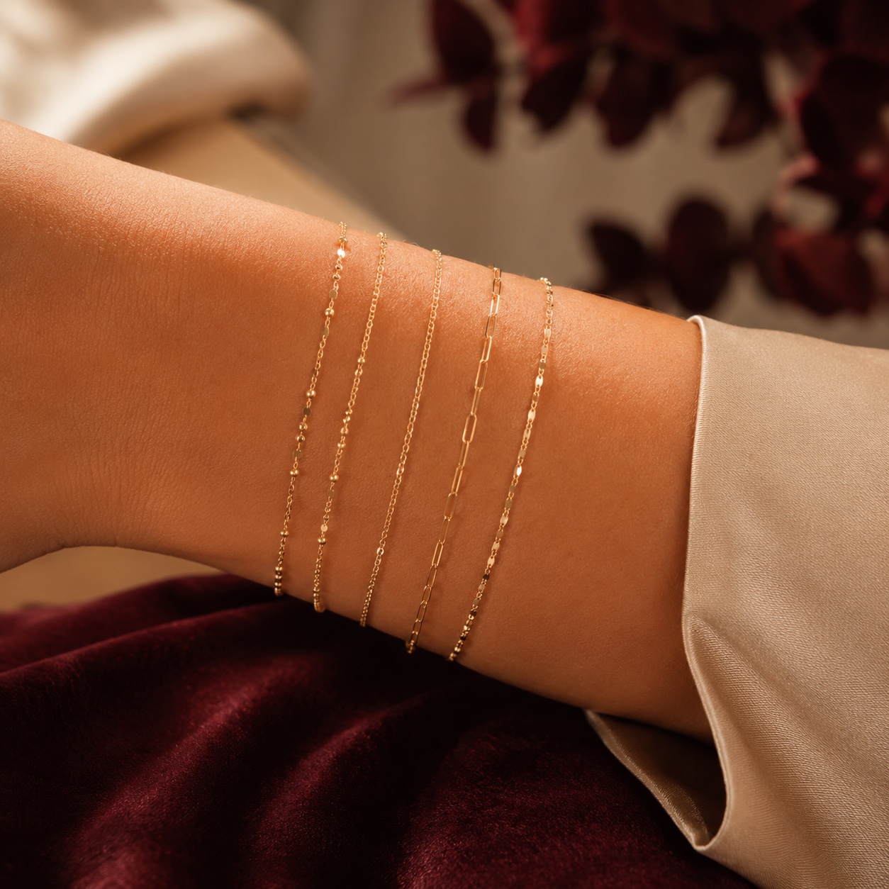 Five delicate gold permanent bracelets styled on a forearm